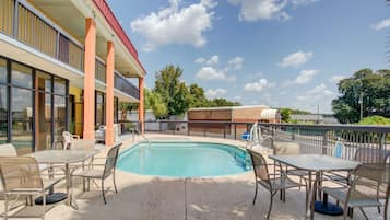 An outdoor pool area with tables and chairs, a building with large windows, and a clear blue sky.