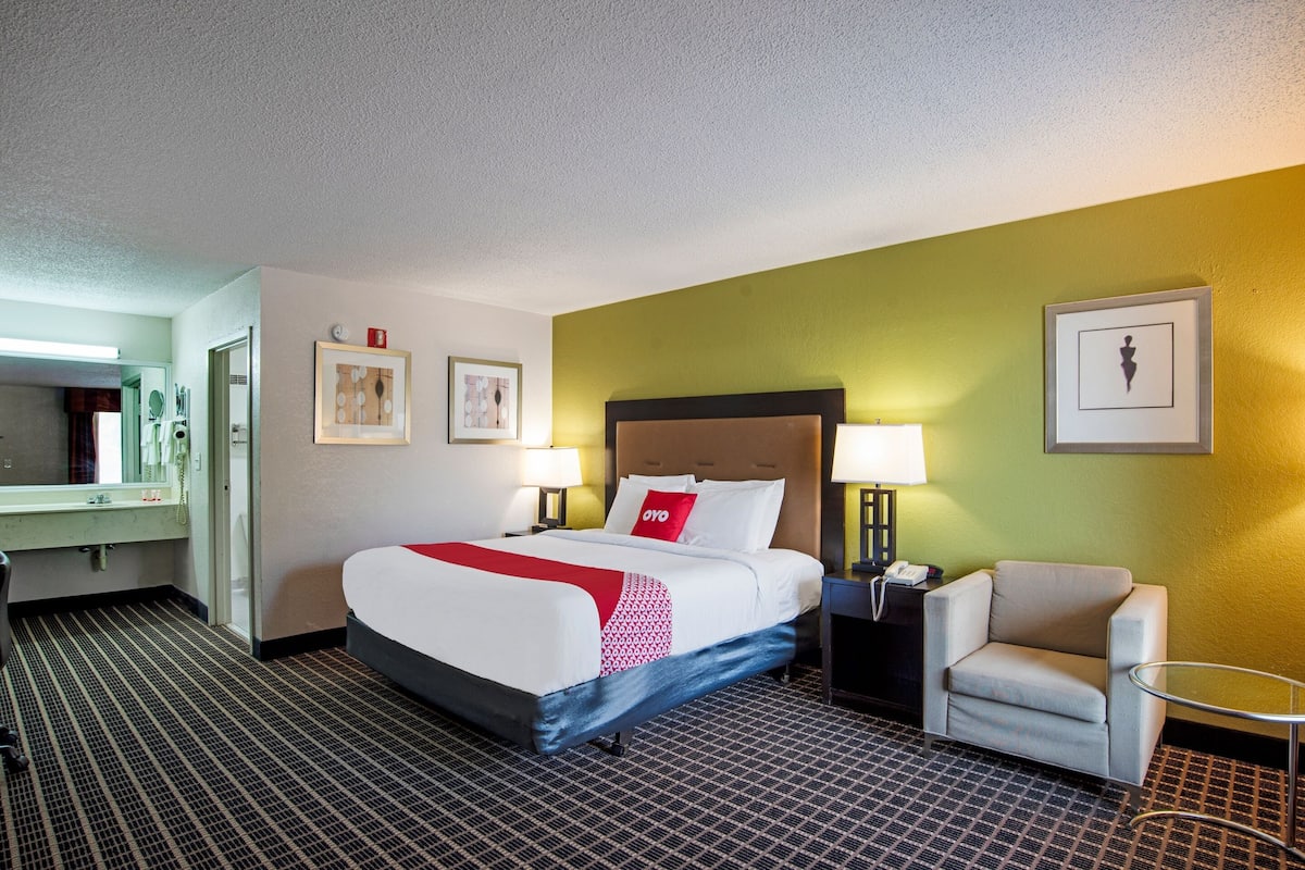 Habitación de hotel con cama, una silla, un escritorio, una lámpara y un cuadro en la pared.