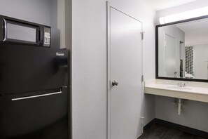 A compact bathroom with a refrigerator, a sink, and a mirror. - Suburban Studios Hinesville - Fort Stewart Area (Hinesville)