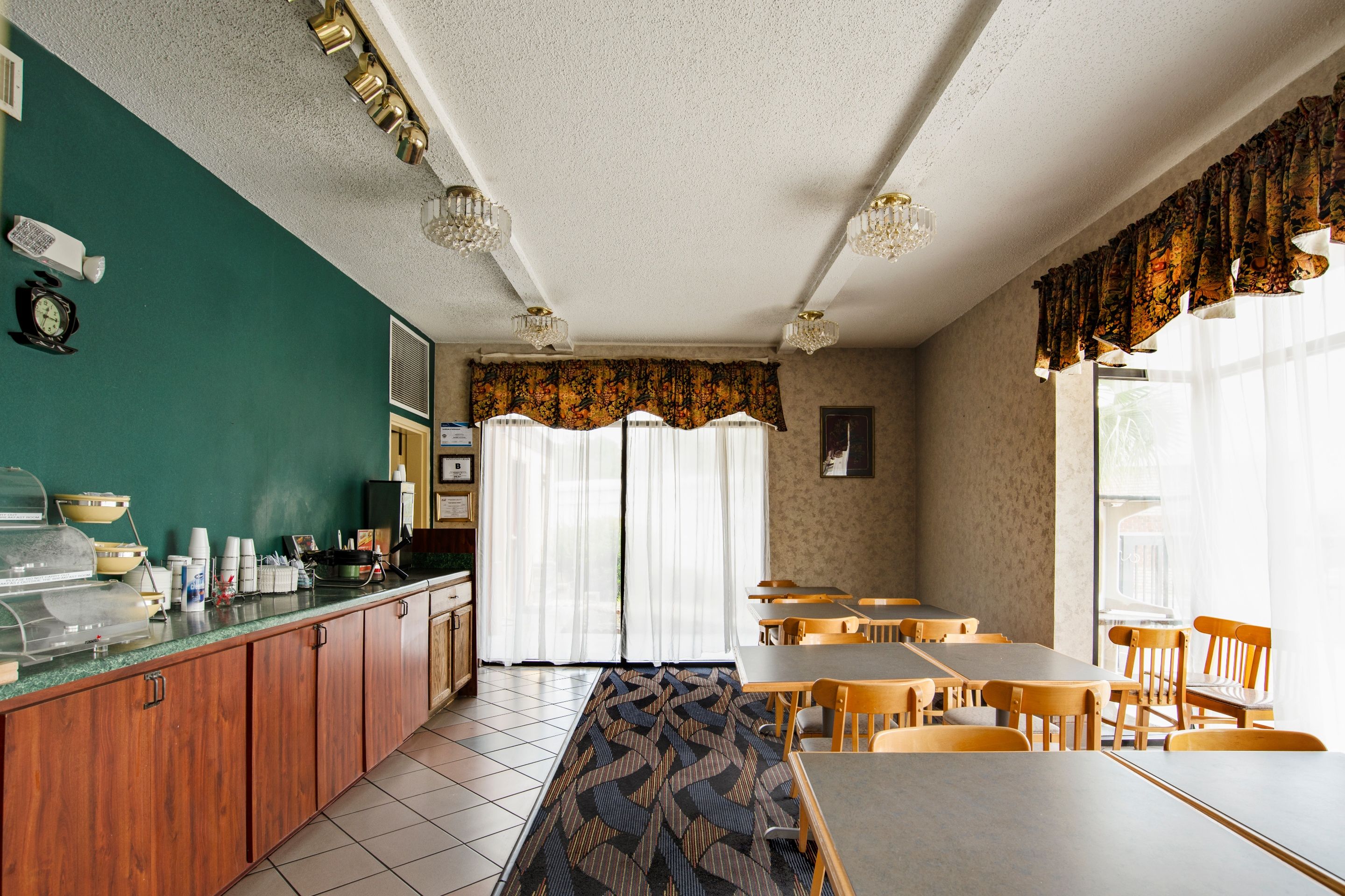 A dining area with tables and chairs, a counter with food containers, and a patterned carpet.