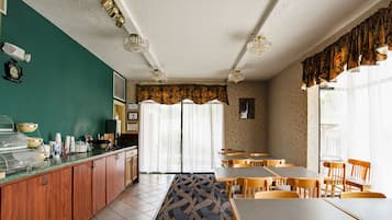 A dining area with tables and chairs, a counter with food containers, and a patterned carpet.