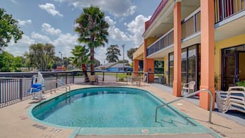 A swimming pool with a lifeguard chair, a palm tree, and a building with balconies and a storefront.