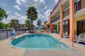 A swimming pool with a lifeguard chair, a palm tree, and a building with balconies and a storefront. - Suburban Studios Hinesville - Fort Stewart Area (Hinesville)