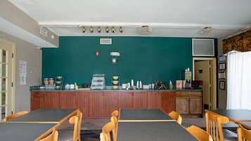 A dining area with wooden tables and chairs, a bar counter with various items, and a green wall.