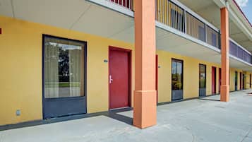 A building with a yellow facade, red doors, and a covered walkway.