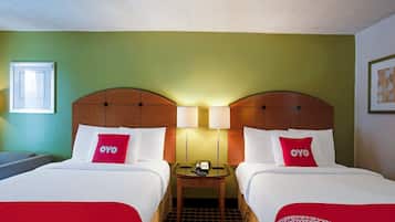 Habitación de hotel con dos camas, cada una con colcha y almohadas rojas y blancas, una mesita de noche con lámpara y un cuadro enmarcado en la pared.