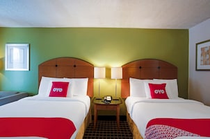 Habitación de hotel con dos camas, cada una con colcha y almohadas rojas y blancas, una mesita de noche con lámpara y un cuadro enmarcado en la pared.