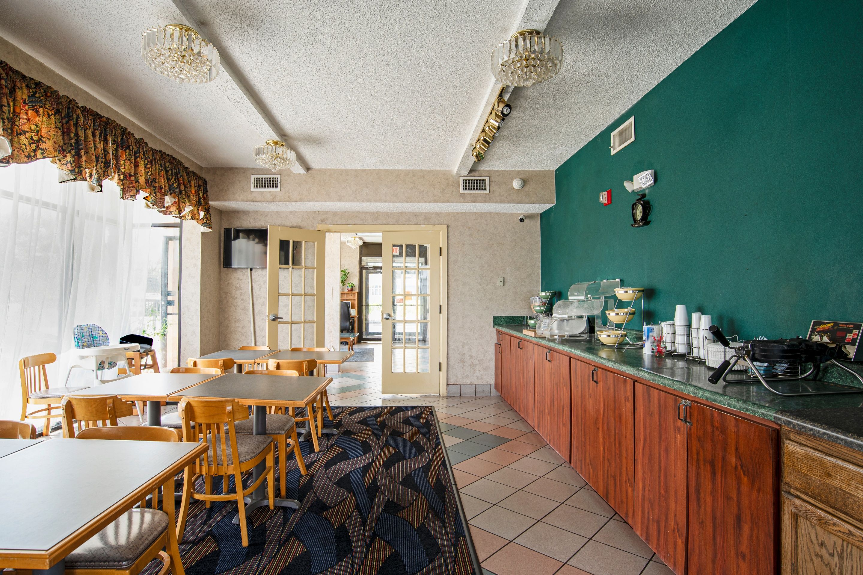 A dining area with wooden tables and chairs, a kitchen counter with appliances, and a green accent wall.