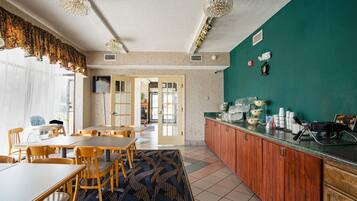 A dining area with wooden tables and chairs, a kitchen counter with appliances, and a green accent wall.