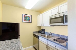 A kitchen with white cabinets, a microwave, a stove, a dishwasher, and a framed picture on the wall. - Mainstay Suites Sterling Near Dulles Town Center (Sterling)