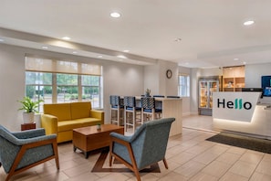 A hotel reception area with a reception desk, seating area with sofas and chairs, a refrigerator stocked with beverages, and a clock on the wall. - Mainstay Suites Sterling Near Dulles Town Center (Sterling)