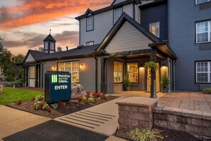 A MainStay Suites building with a sign indicating the entrance, a covered walkway, and a landscaped area with plants. - Mainstay Suites Sterling Near Dulles Town Center (Sterling)