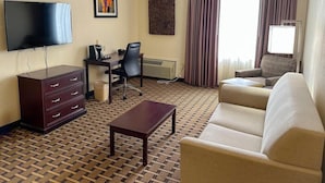 A hotel room with a flat-screen TV, a desk with a chair, a sofa, a coffee table, and a patterned floor. - Sonesta Essential Hotels Overland Park (Overland Park)