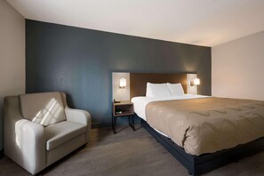 A hotel room with a bed, a chair, a nightstand, and wall-mounted lamps. - Quality Inn University Area Farmville, VA (Farmville)