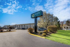 Entrada de un hotel con un cartel de Quality Inn by Choice Hotels, un estacionamiento y un edificio con un corredor cubierto.