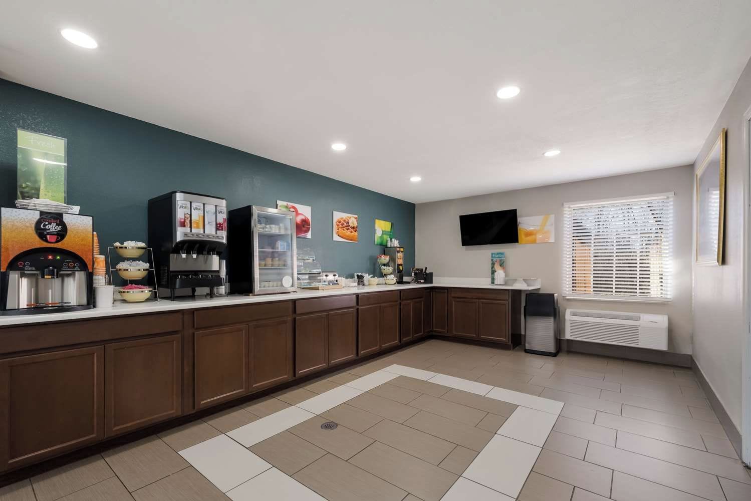 A modern kitchen with a coffee station, a refrigerator, and a flat-screen TV mounted on the wall.