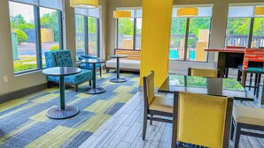 A hotel lobby with large windows, a seating area with tables and chairs, and a pool view. - OYO Townhouse Jackson/ridgeland (Jackson)