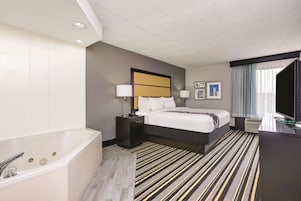 Habitación de hotel con una cama grande, un baño independiente con bañera, un escritorio con computadora y una ventana con cortinas.