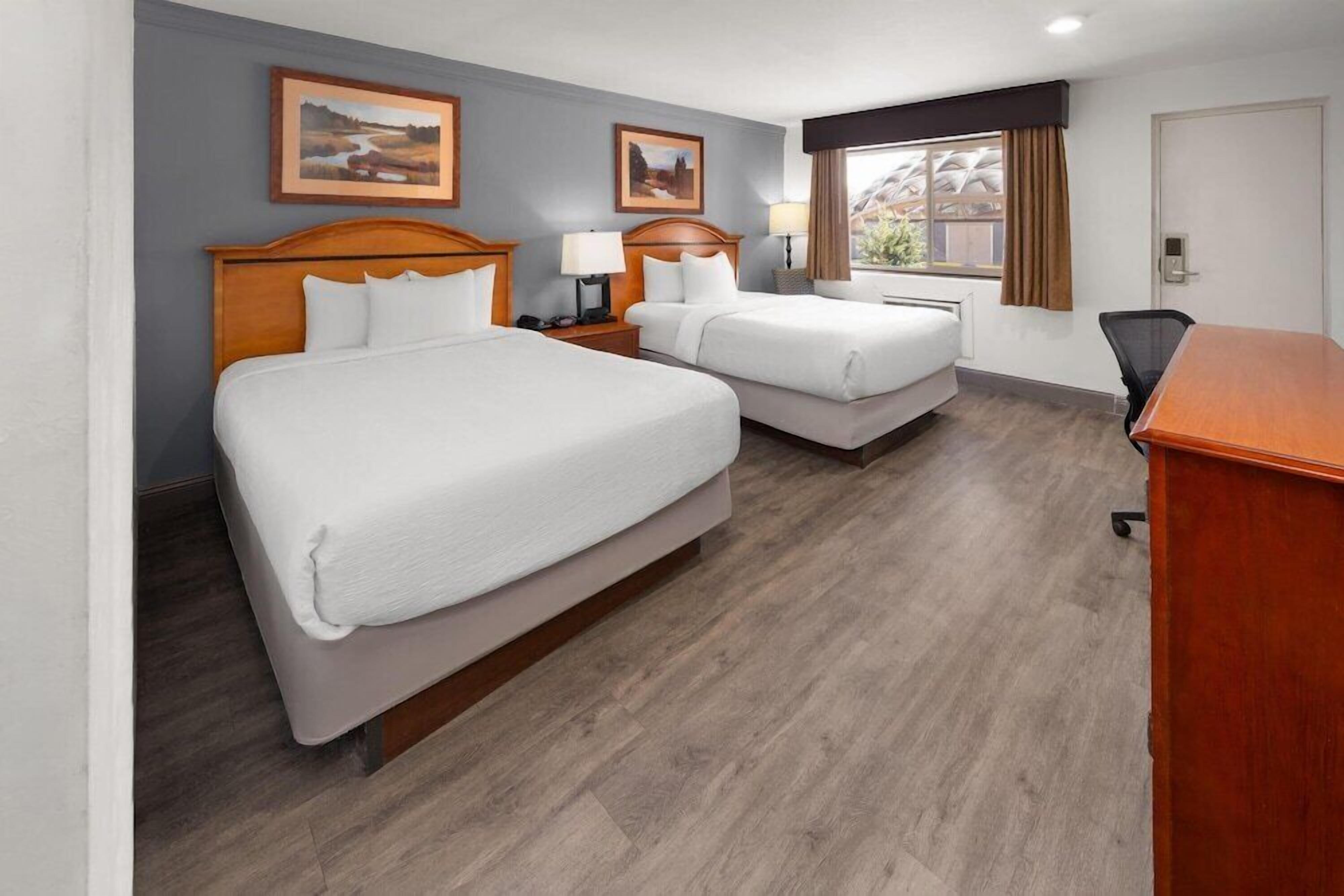 A hotel room with two beds, a desk, and a window with curtains.