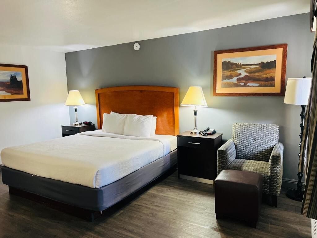 A hotel room with a large bed, two bedside tables with lamps, a chair, and two framed pictures on the wall.