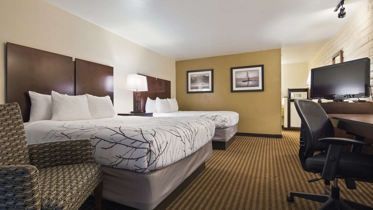 Habitación de hotel con dos camas, un escritorio, una silla, un televisor y dos cuadros en la pared.