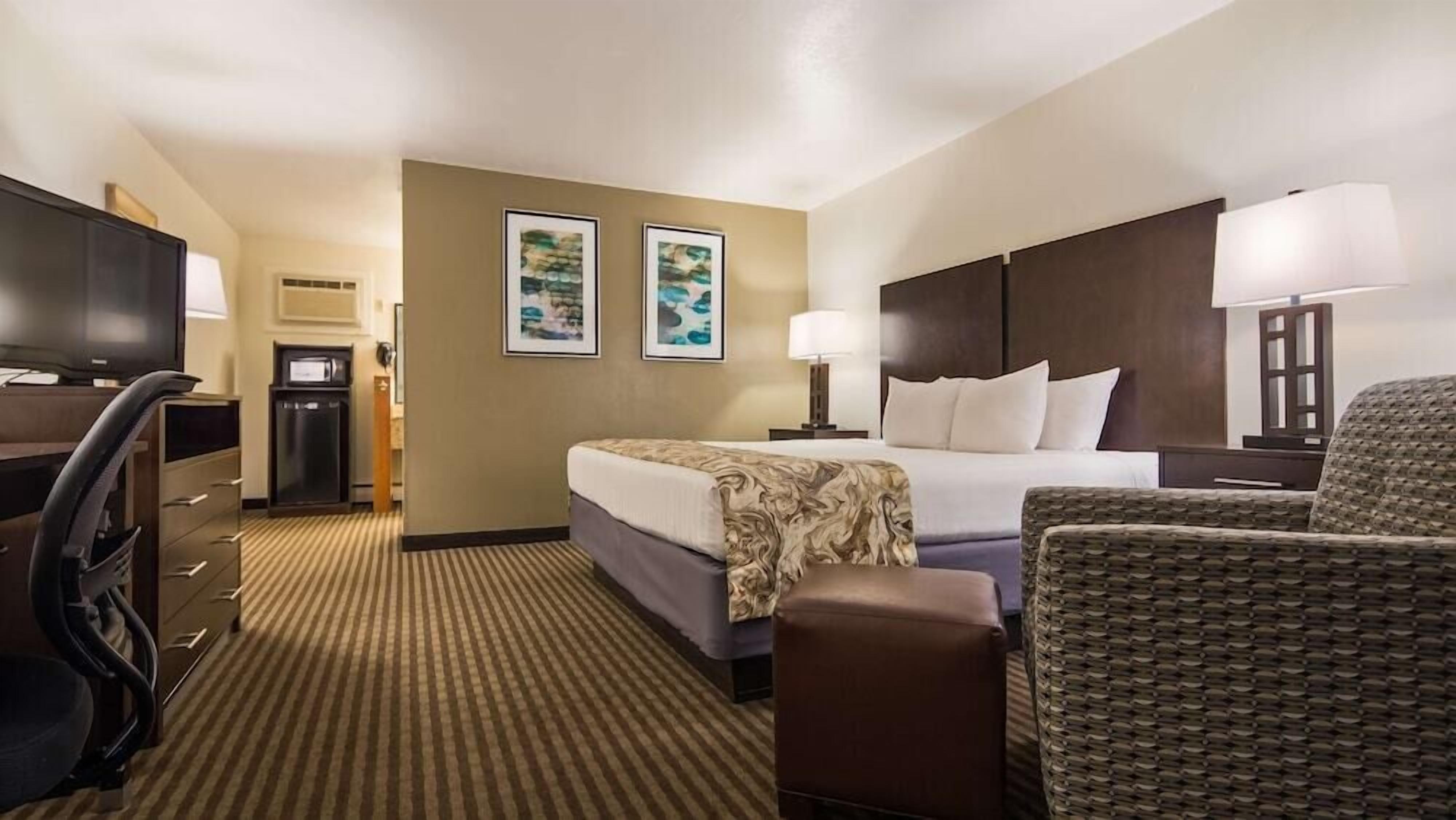 A hotel room with a bed, a desk, a chair, a television, and two framed pictures on the wall.