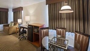 Une chambre d’hôtel avec un canapé, un bureau avec un ordinateur, une table en verre et un coin repas avec des chaises.