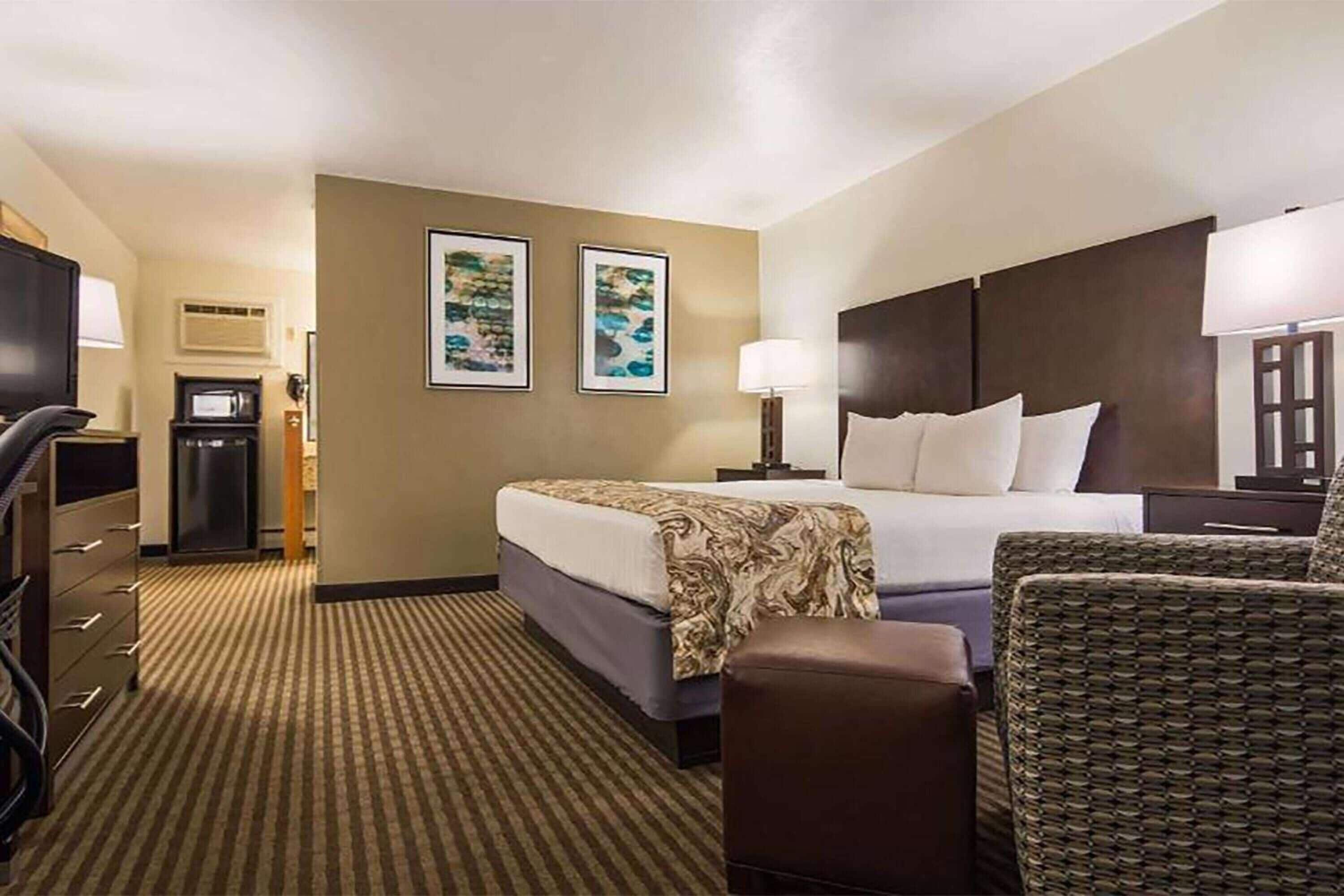 A hotel room with a bed, a chair, a desk, a television, and two framed pictures on the wall.