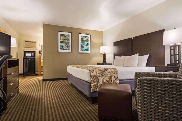 A hotel room with a bed, a chair, a desk, a television, and two framed pictures on the wall.