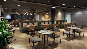 Un restaurant moderne avec des sièges verts, des tables rondes et des luminaires suspendus.