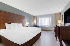 A hotel room with a large bed, a desk, a chair, a TV, and an air conditioning unit. - Clarion Hotel & Suites BWI Airport North (Baltimore)