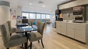A modern hotel room with a dining area, an ATM, a coffee machine, and a view of the city. - Clarion Hotel & Suites BWI Airport North (Baltimore)