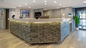 A reception area with a stone-textured counter, a clock, and a framed cityscape poster. - Clarion Hotel & Suites BWI Airport North (Baltimore)