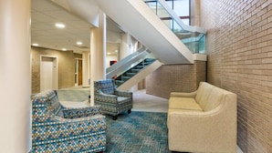 A lobby with a staircase, patterned chairs, and a beige sofa. - Clarion Hotel & Suites BWI Airport North (Baltimore)