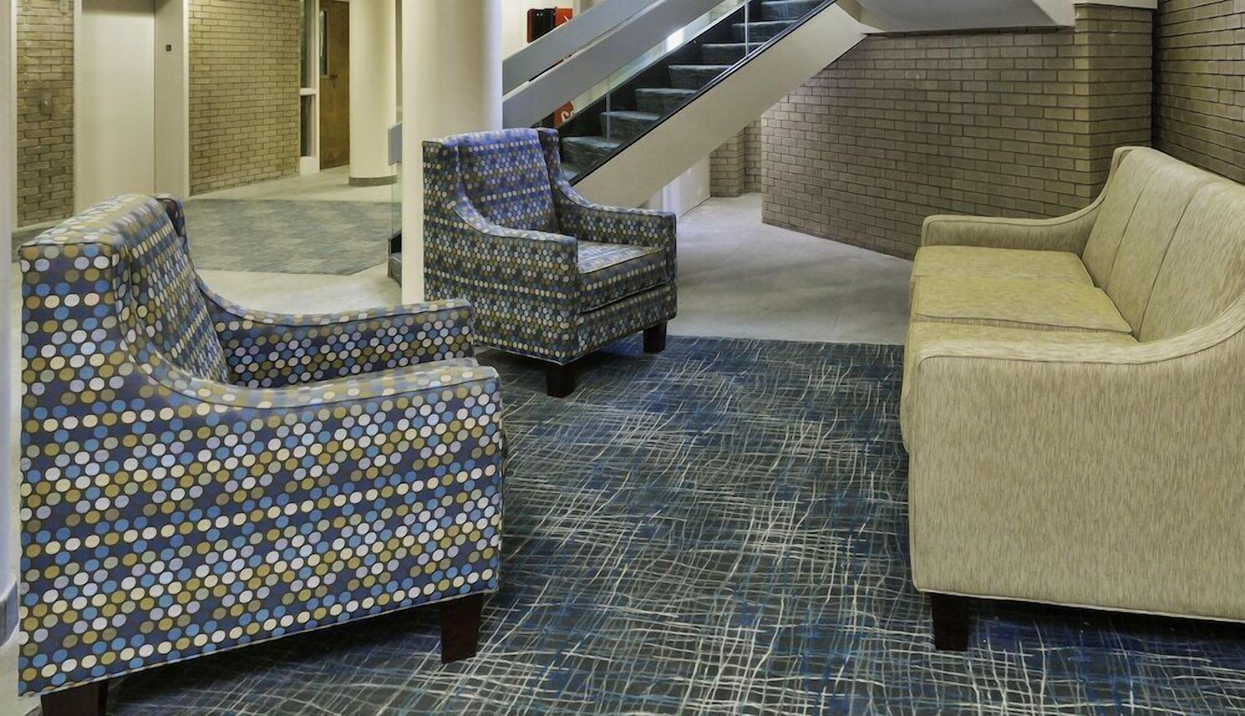 Un hall con un sillón azul estampado, un sillón estampado y un sofá beige.