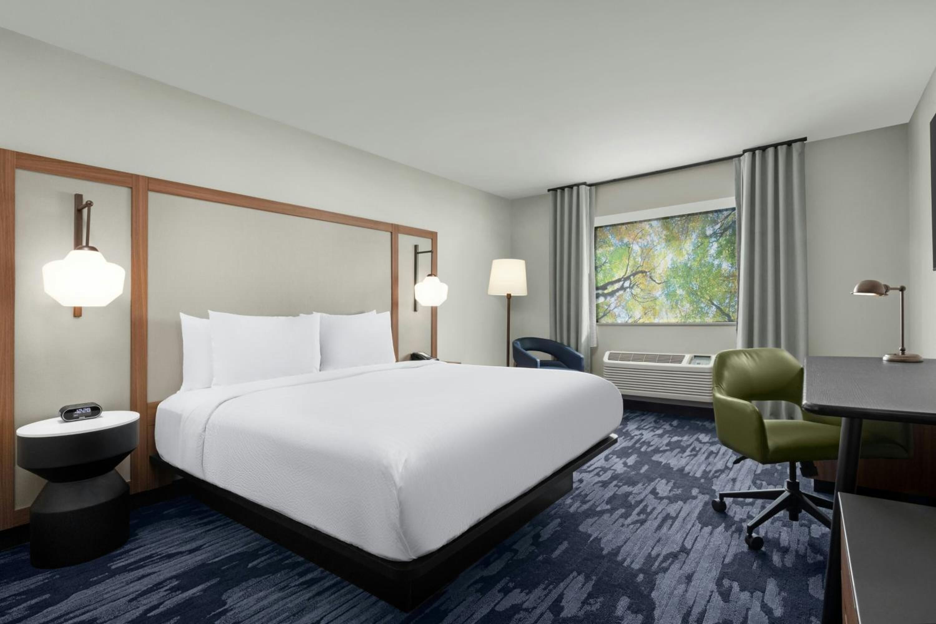 A hotel room with a large bed, a desk, a chair, and a window with curtains.