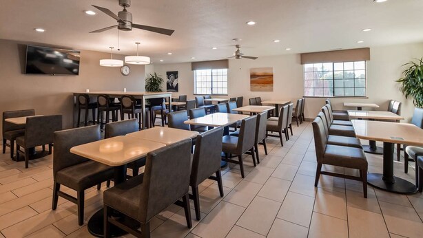 A spacious dining area with multiple tables and chairs, ceiling fans, and large windows providing natural light. - Colony Inn Hotel Atascadero (Atascadero)