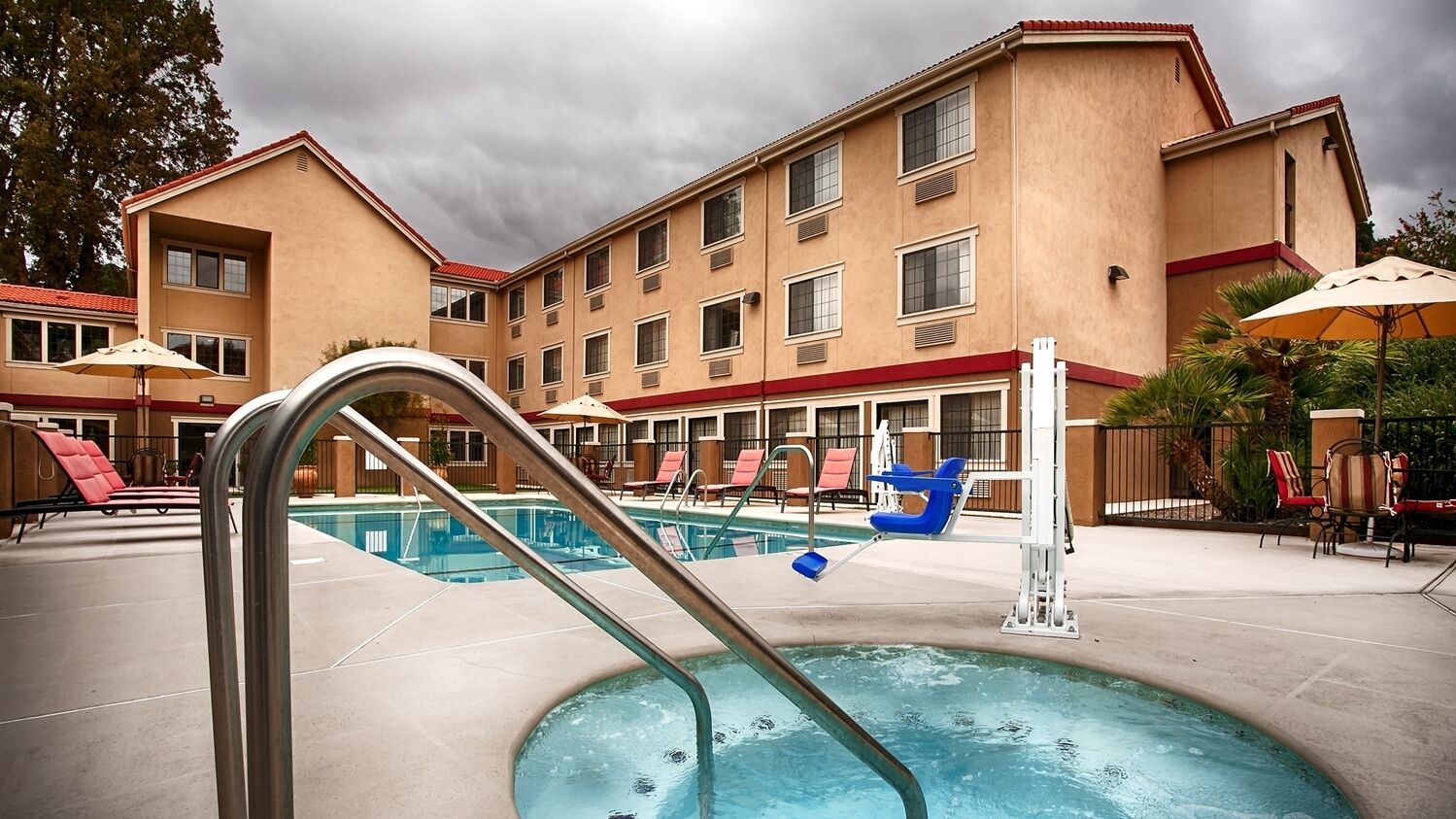 A hotel pool area with a pool, lounge chairs, and umbrellas.