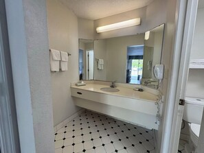 A bathroom with a white sink, a large mirror, and a black and white tiled floor. - Super 8 By Wyndham Savannah (Savannah)