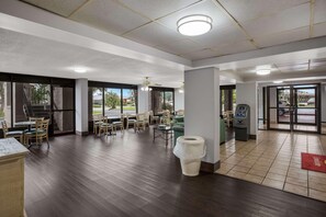 A spacious indoor area with a large window, a restroom, and a seating area with tables and chairs. - Super 8 By Wyndham Savannah (Savannah)