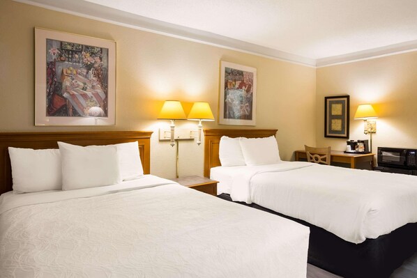 A hotel room with two beds, two wall-mounted lamps, a desk with a chair, a television, and two framed pictures on the wall. - Super 8 By Wyndham Savannah (Savannah)