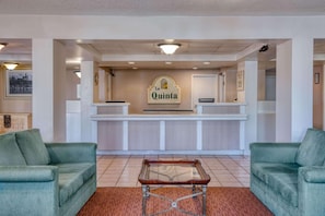 A reception area with a sign reading 'la Quinta,' two green sofas, a glass-top table, and a tiled floor. - Super 8 By Wyndham Savannah (Savannah)