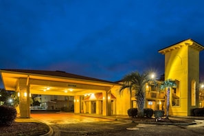 Un hotel con entrada cubierta, una palmera y una fachada bien iluminada.