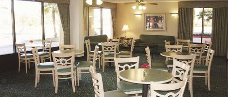 Une chambre d’hôtel dotée d’un coin repas, de plusieurs chaises, d’une table, de ventilateurs de plafond et de grandes fenêtres.