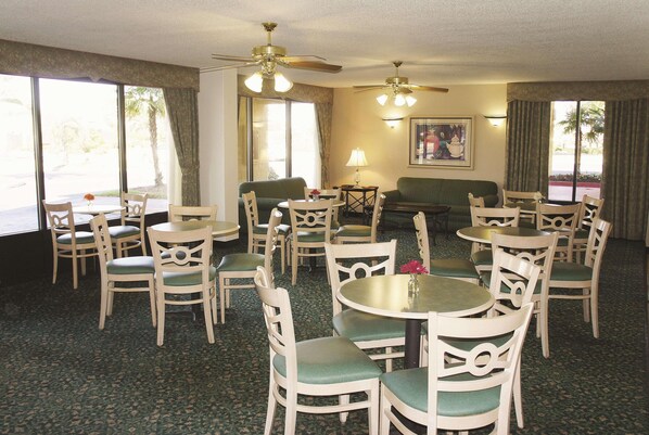Une chambre d’hôtel dotée d’un coin repas, de plusieurs chaises, d’une table, de ventilateurs de plafond et de grandes fenêtres.