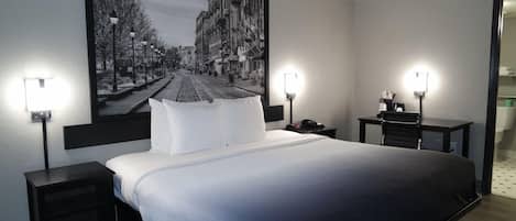Et hotelværelse med en stor seng, to sengeborde, et skrivebord og et TV på væggen.