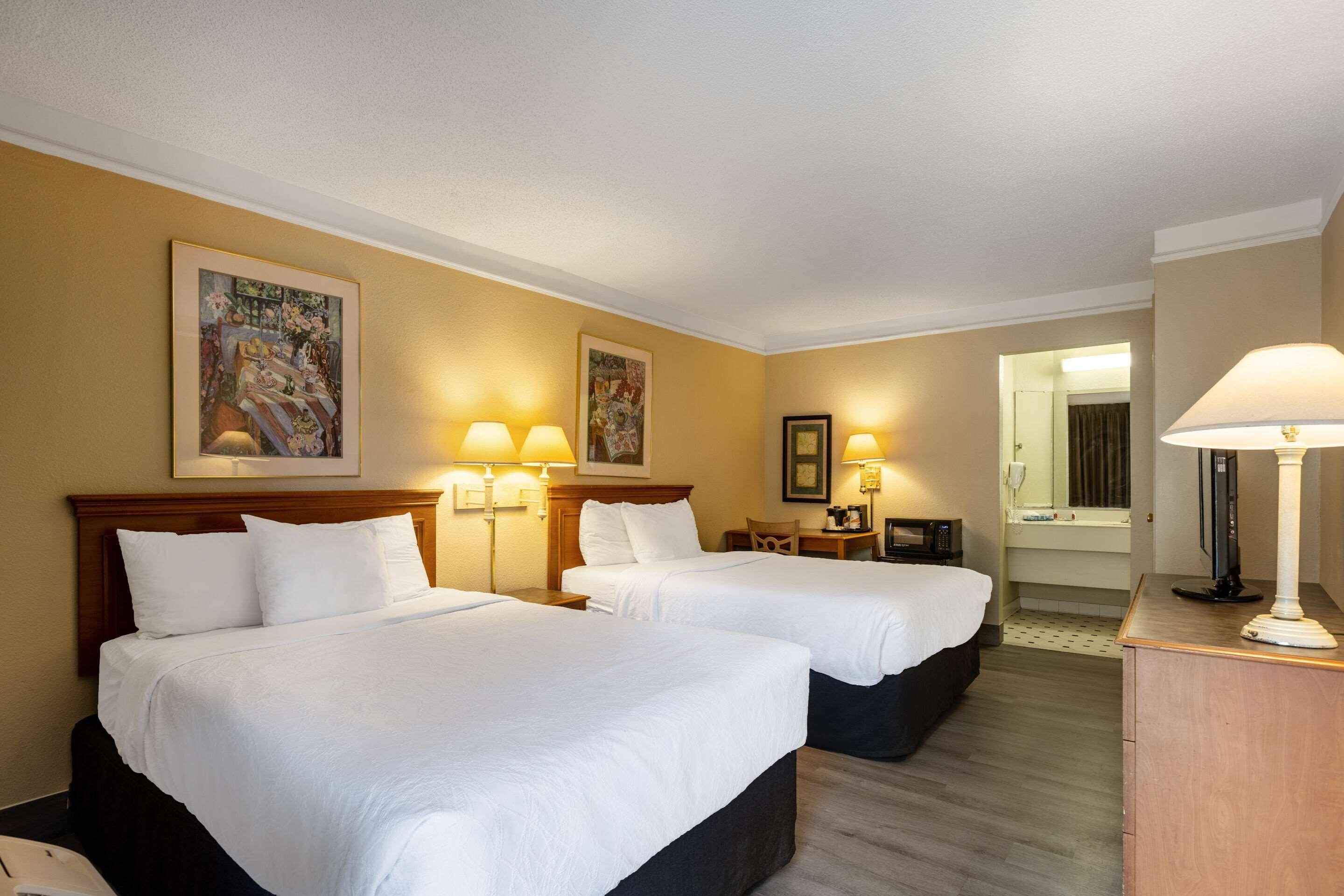 Ein Hotelzimmer mit zwei Betten, einem Schreibtisch, einem Stuhl, einer Lampe und einem Spiegel.