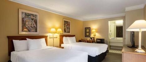 Habitación de hotel con dos camas, un escritorio, una silla, una lámpara y un espejo.
