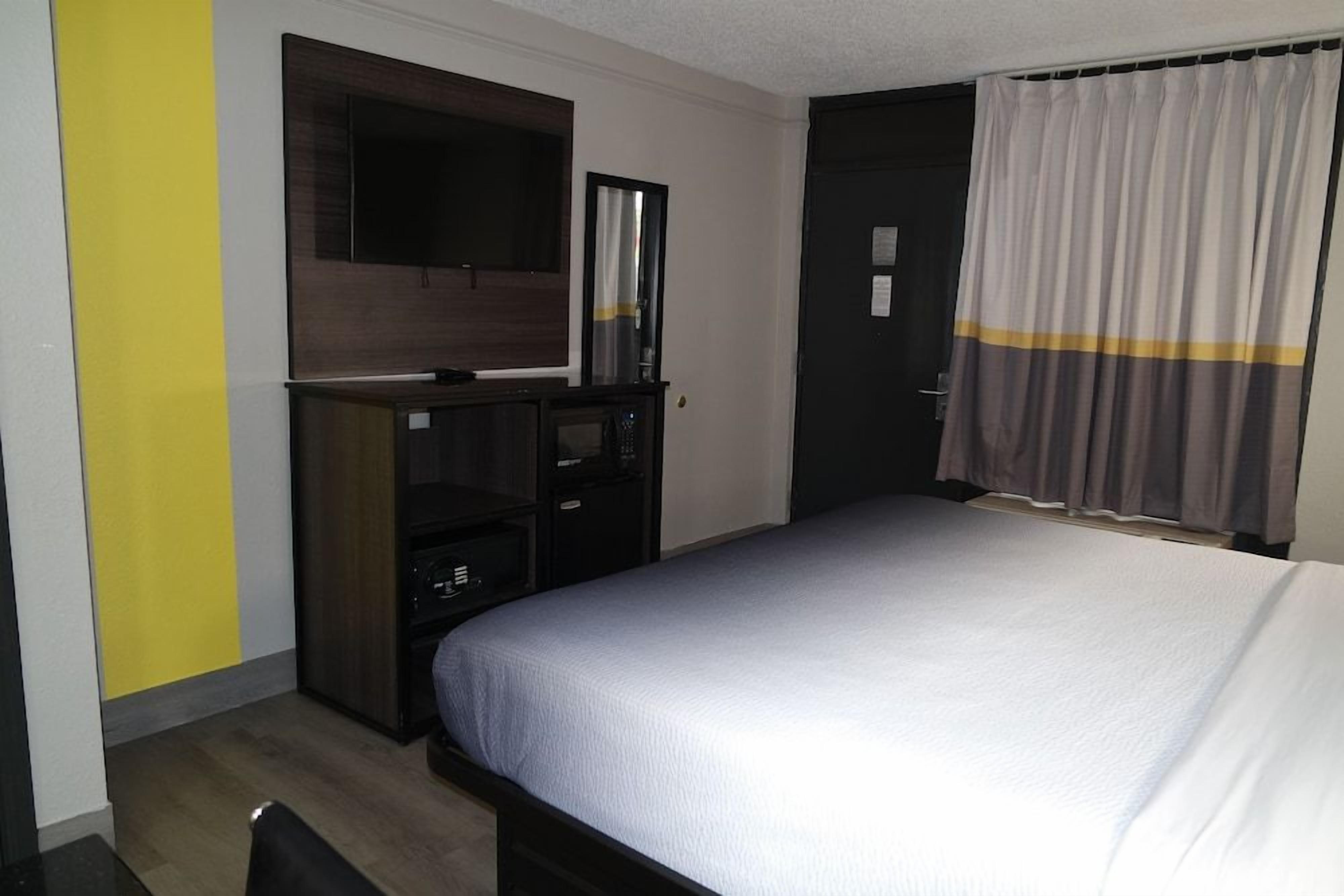 A hotel room with a bed, a TV mounted on the wall, a wardrobe, and a door with a curtain.
