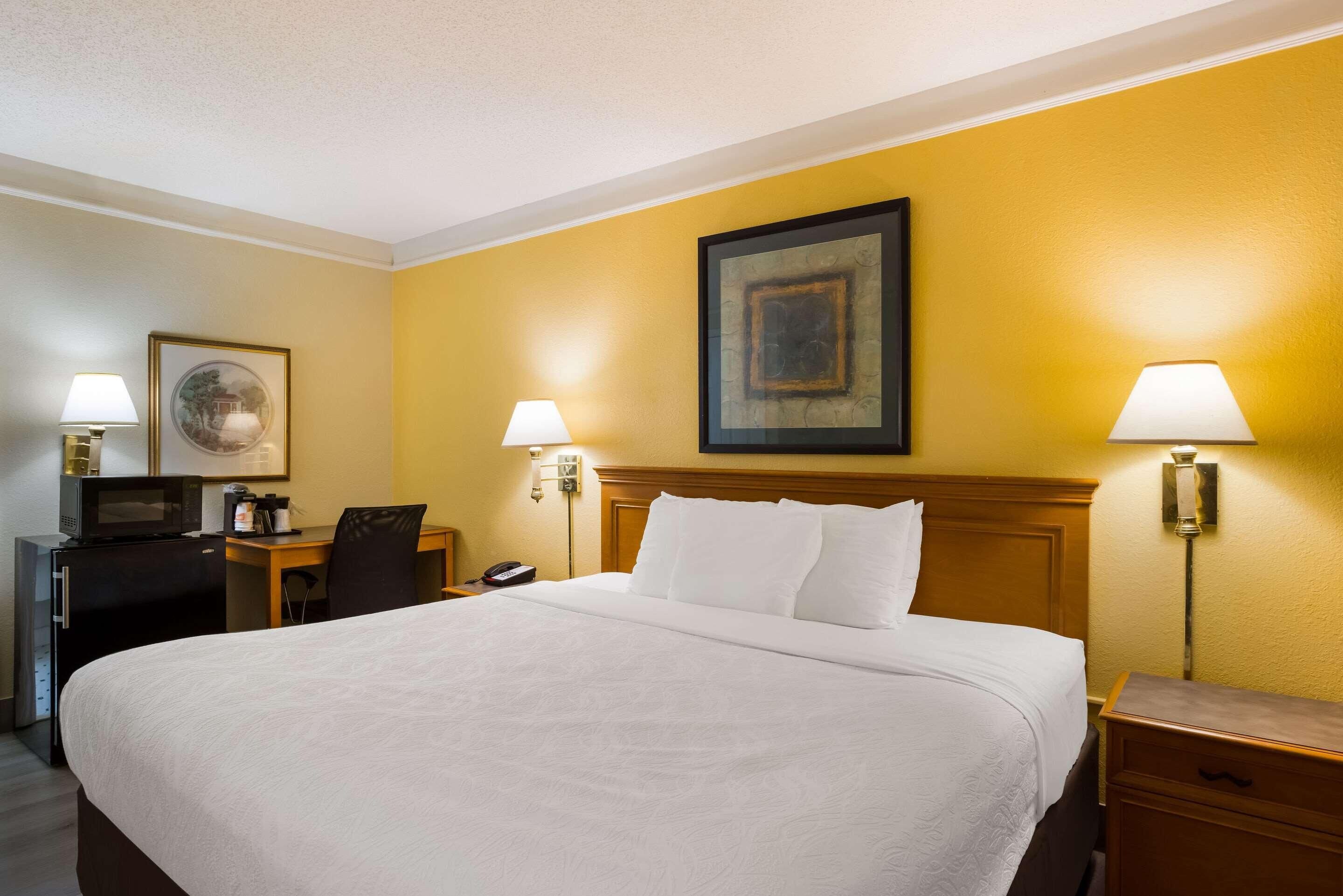 A hotel room with a large bed, a desk with a computer, a telephone, and two wall-mounted lamps.